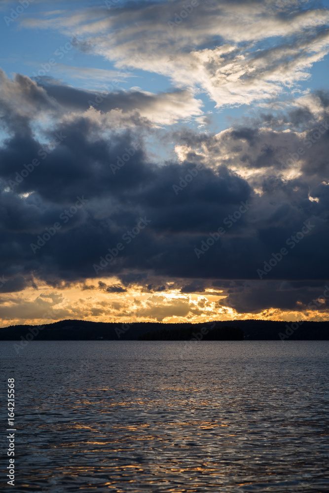 View of dark and dramatic clouds and a lake at sunset in Finland in the summer.