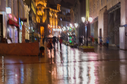 Blurred background of young people walking down street in rainy evening, Impressionism style, colorful lighting. Intentional motion blur. Concept of seasons, weather, modern city.