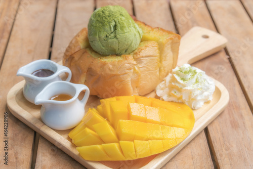 Fototapeta Naklejka Na Ścianę i Meble -  Honey toast green tea ice scream with ripe barracuda mango and whipping cream in wooden plate on wooden table.