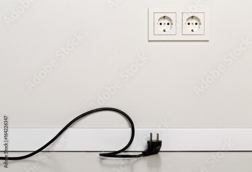 Black power cord cable unplugged with european wall outlet on white plaster wall photo