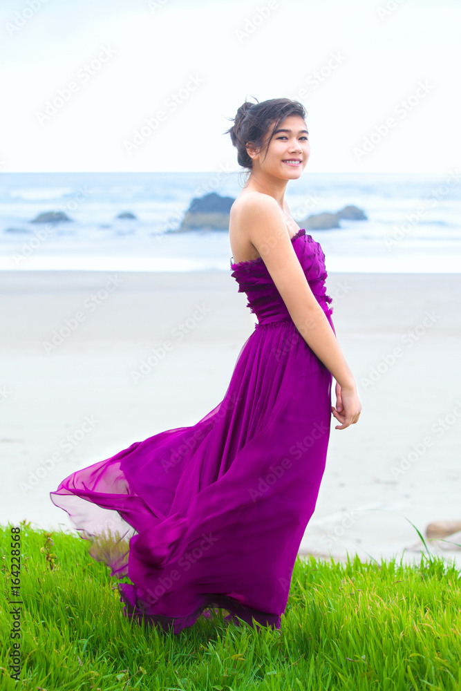 Teen girl wearing purple gown on grassy knoll overlooking ocean Teen girl wearing purple gown on grassy knoll overlooking ocean