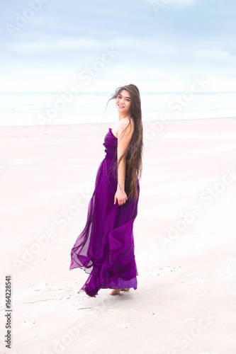 Teen wearing purple dress on beach looking back over shoulder