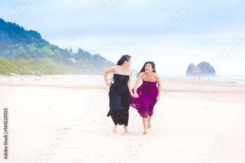 Two teenager girls running on beach on cool cloudy day