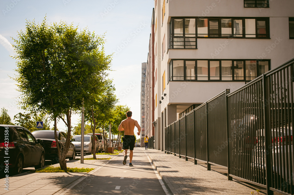 Handsome sexy male bodybuilder athlete man with naked torso, Morning run in open air in urban courtyards, early sunny summer morning. Healthy lifestyle concept.