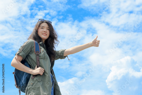 Tourist asian woman hitchhiking on the blue sky background