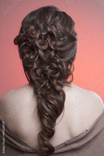 Demonstration of hairstyles Greek braid on the back of brown hair and clean skin isolated on light pink background. Close-up. Makeup Nude.