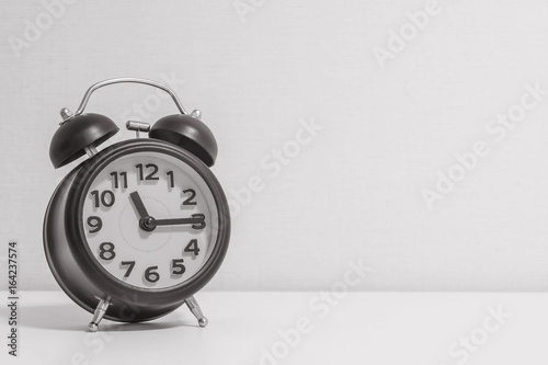 Closeup alarm clock for decorate show a quarter past eleven o'clock or 11:15 a.m.on white wood desk and cream wallpaper textured background in black and white tone with copy space