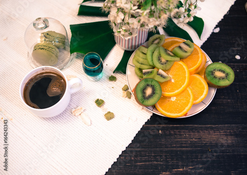 Morning tea or coffee with orange and kiwies slices and green macaroons on a white blanket with cherry blossom photo