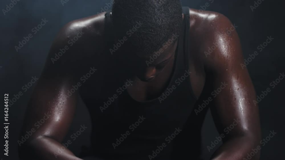 Portrait shot of a muscular black man resting in between workouts on a foggy dark background.