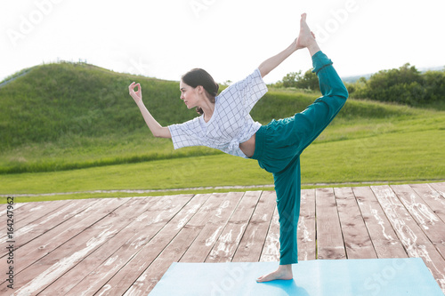 Woman doing yoga outdoor. Young woman exercising vital and meditation for fitness lifestyle at the nature background in green park on wooden platform. Concept Yoga freedom