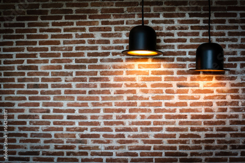 Black lamps is shining orange light on red brick wall for background texture.