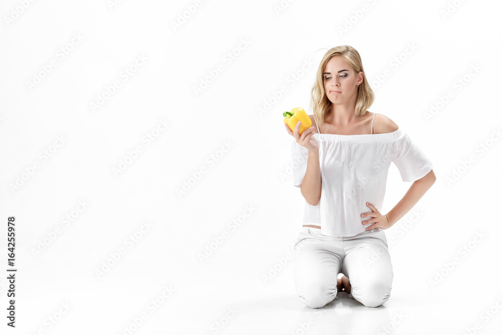 Beautiful serious blonde woman in white blouse looks at yellow bell pepper. Healthy eating and diet Beautiful serious blonde woman in white blouse looks at yellow bell pepper. Healthy eating and diet