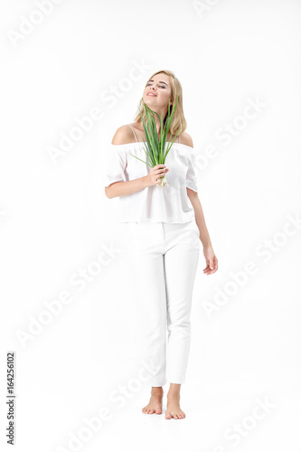 Beautiful blond woman in white blouse holding green onion on white background. Health and vitamins