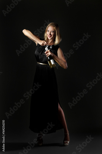 Beautiful blonde woman holding white wine bottle on black background. Party and holiday