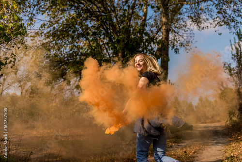 Happy girl laughs and works with the orange color of a smoke bomb in the forest.