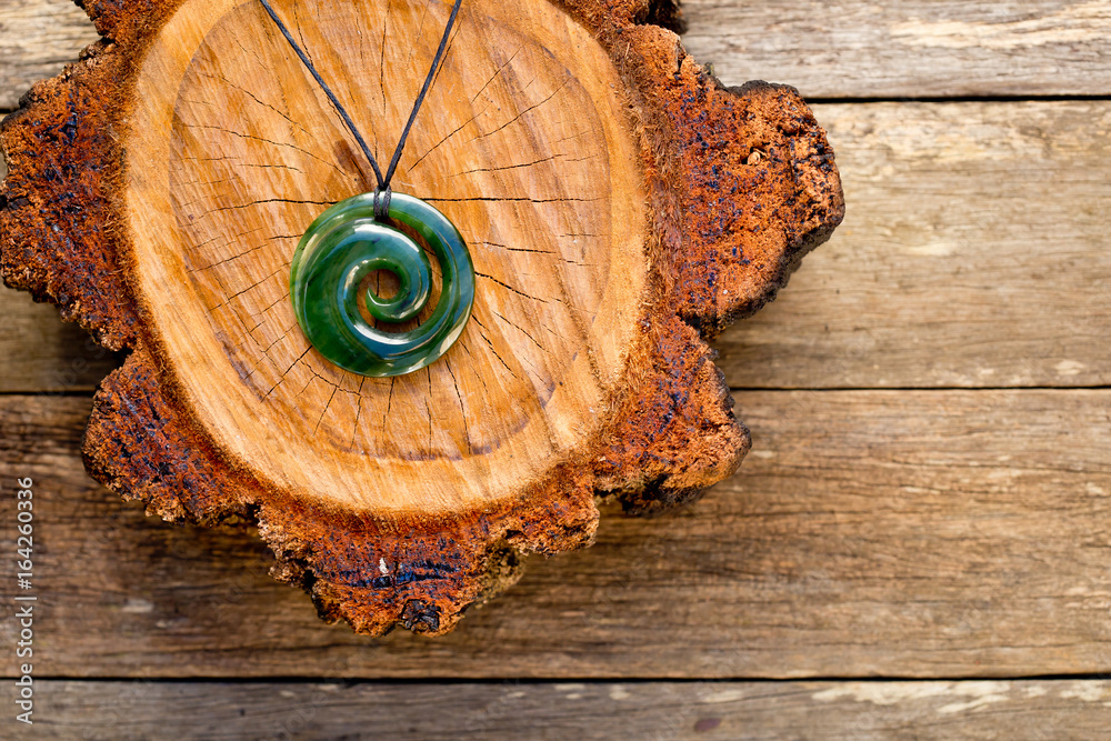 Fototapeta premium Maori New Zealand Greenstone pounamu jade Koru (spiral fern) shape pendant on cross section of timber log