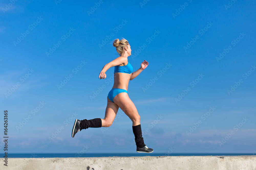 Jogging. Young sportswoman in blue sportswear runs along seafront
