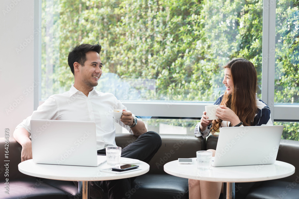 Two asian coworkers use laptop work together having coffee in afternoon Two asian coworkers use laptop work together having coffee in afternoon