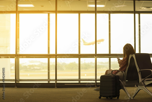 Young beautiful woman in airport with travel bag use smartphone at airport wait for flight, world exploration concept