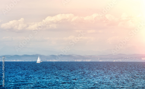 Seascape with a lone white sailboat in the distance.
