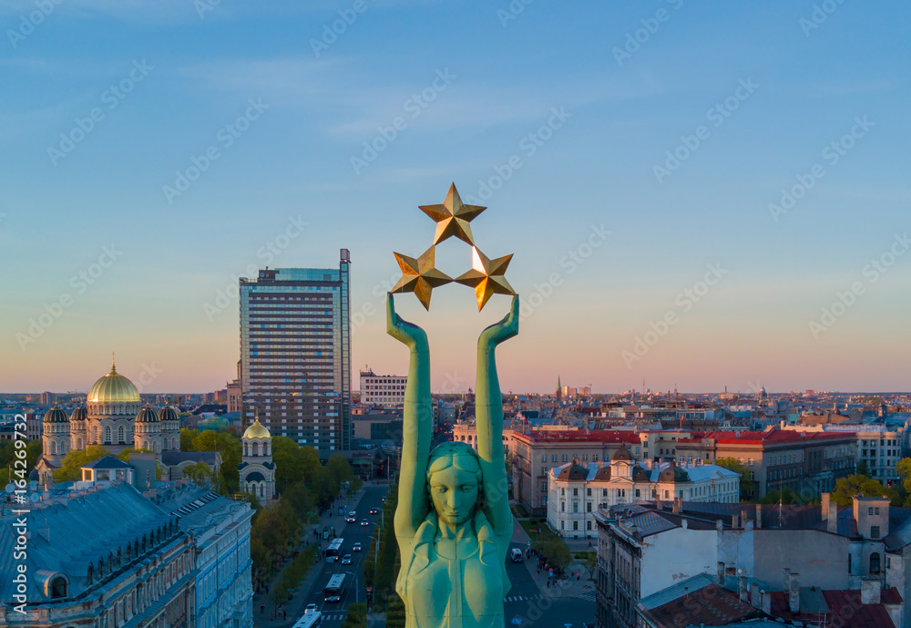 Beautiful sunset view in Riga by the statue of liberty - Milda. Freedom in Latvia. Statue of liberty holding three stars over the city. Latvian spirit. - obrazy, fototapety, plakaty 