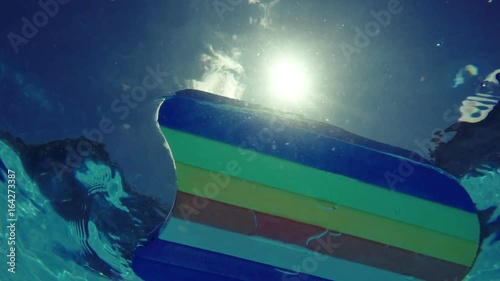 Rainbow pattern styrofoam swimming board floating in swimming pool water, summertime vacation recreational activity object in the poolside, underwater view photo