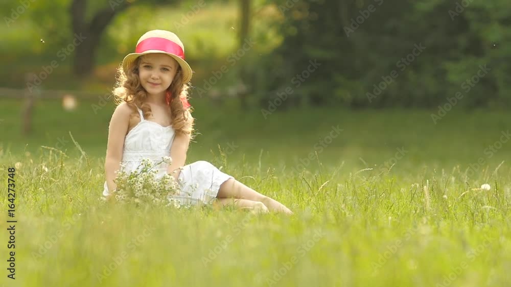 Baby sits on a glade in a sarafan and hat, holds wild flowers and smiles. Slow motion Baby sits on a glade in a sarafan and hat, holds wild flowers and smiles. Slow motion