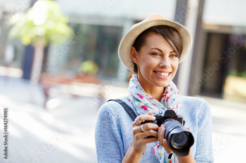 Outdoor summer smiling lifestyle portrait of pretty young woman with camera