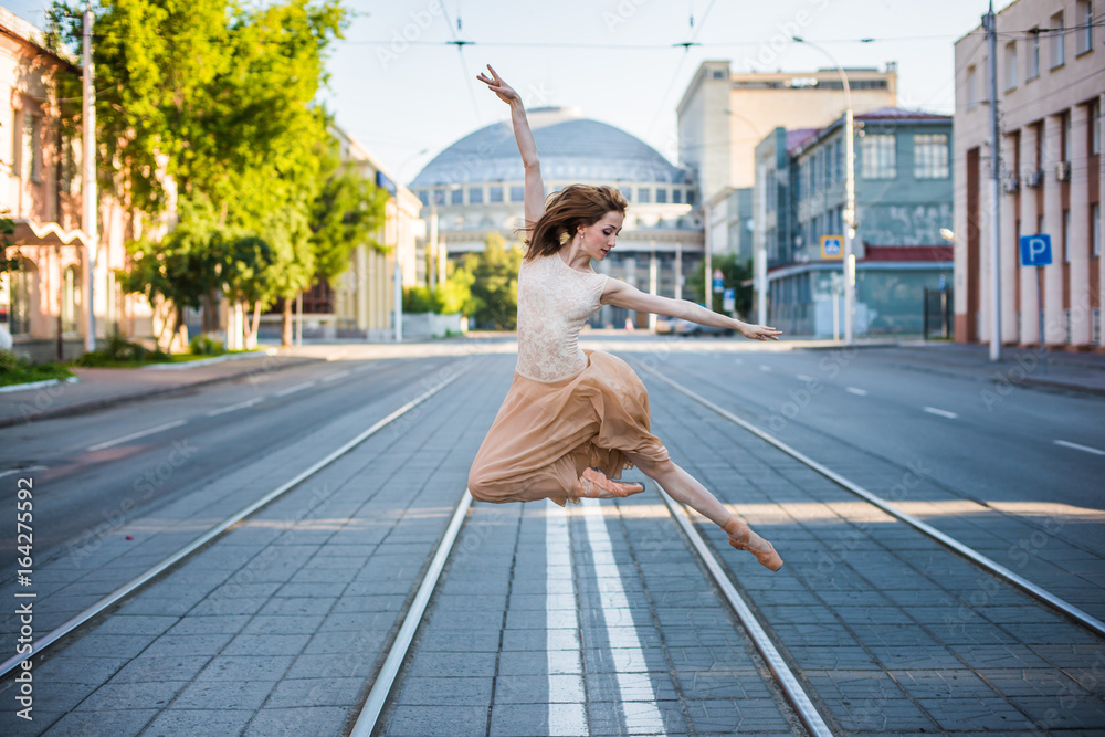Obraz premium Ballerina in leotard and skirt and ballet shoes dancing on the street, jumps and bends