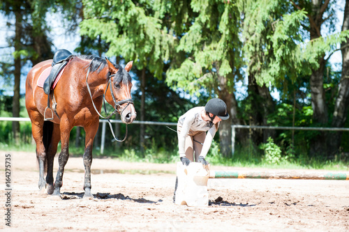 Teenage girl equestrian at horseriding school manege preparing obstacles