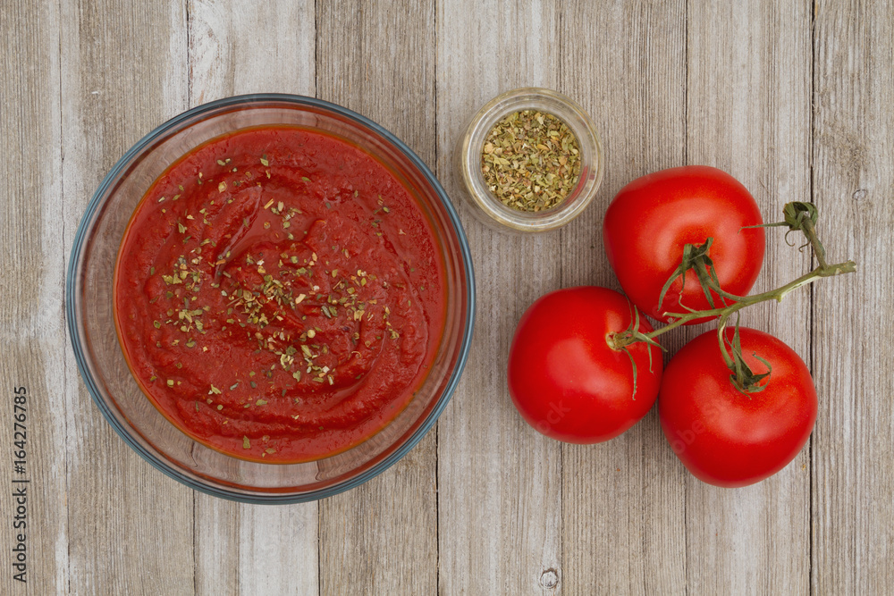 Tomato sauce in clear bowl with oregano spice and red vine ripe tomatoes on weathered wood background Tomato sauce in clear bowl with oregano spice and red vine ripe tomatoes on weathered wood background