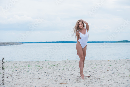 beautiful slim girl in white swimsuit posing on the beach in cloudy weather 
