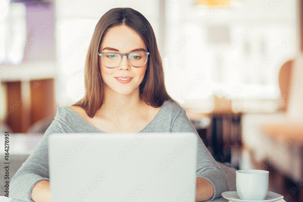 Smiling teenage girl sitting at laptop in cafe Smiling teenage girl sitting at laptop in cafe
