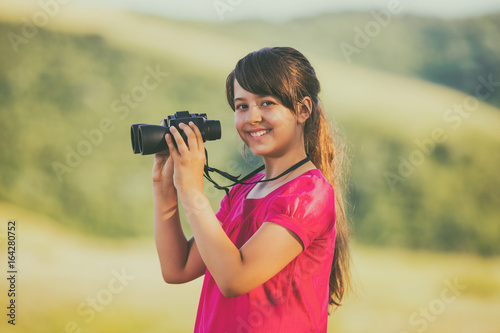 Beautiful little girl enjoys in nature with binoculars.