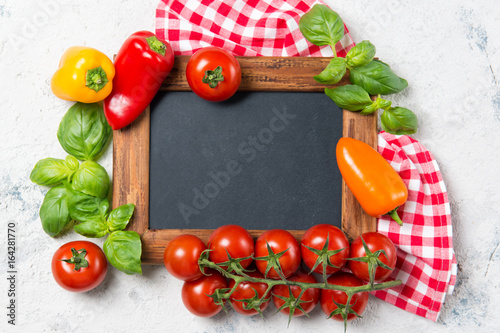 Ripe cherry tomatoes, mini bell peppers, fresh basil leaves on stone table with chalkboard, cooking ingredients top view