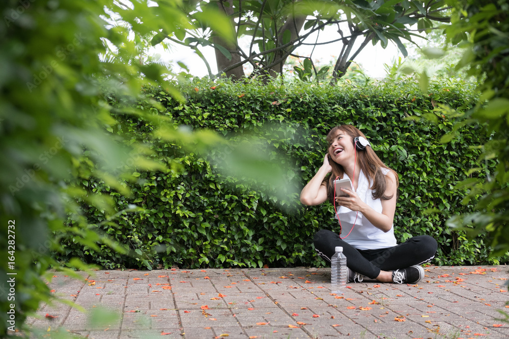 Naklejka premium asian woman with headphones. young female holding mobile smart phone. a girl listening to music in public park