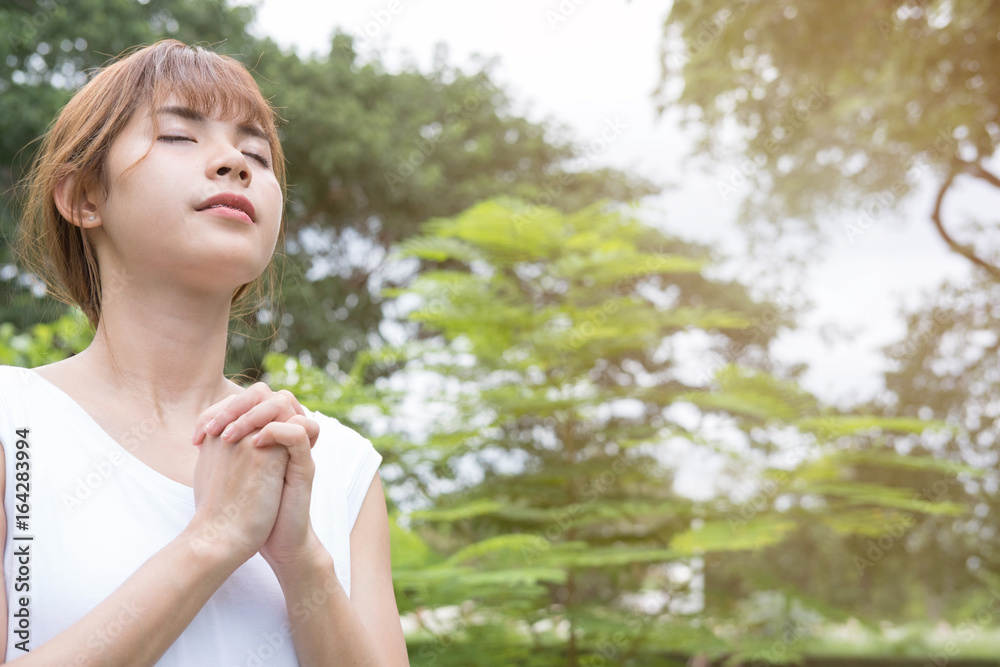 Young woman praying in public park. asian girl folded her hands in prayer Young woman praying in public park. asian girl folded her hands in prayer