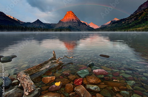 "Morning Glory" Sunrise lights up the top of Sinopah Mountain in Glacier National Pk. The mountain and rainbow are reflected in the still waters of Two Medicine Lake 
