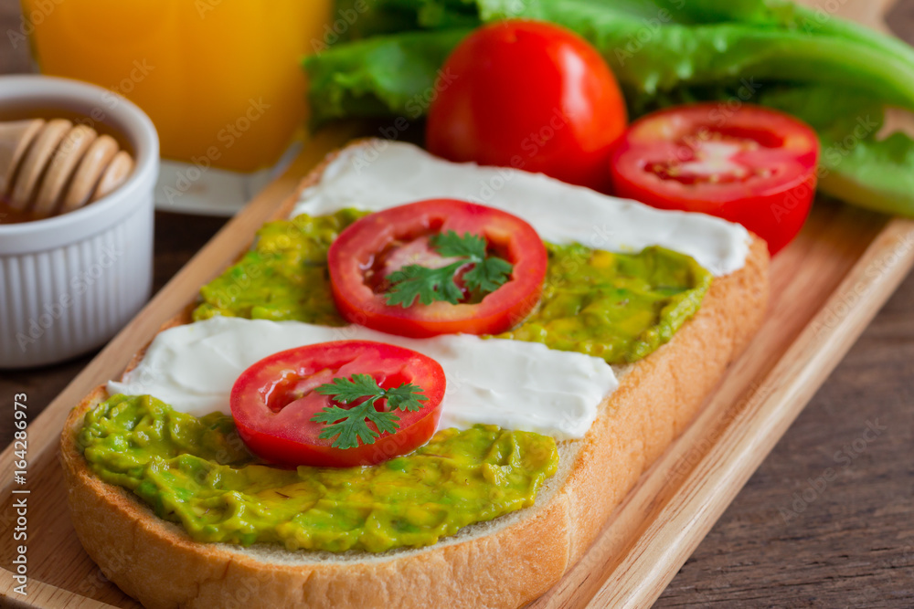 Open sandwich for breakfast or lunch. Sandwich spread with cream cheese, avocado and tomato.Avocado and cream cheese open sandwich style serve with orange juice on rustic wood table in close up view. Open sandwich for breakfast or lunch. Sandwich spread with cream cheese, avocado and tomato.Avocado and cream cheese open sandwich style serve with orange juice on rustic wood table in close up view.