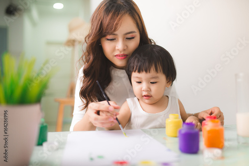 Happy family mother and daughter together paint. Asian woman helps her child girl.