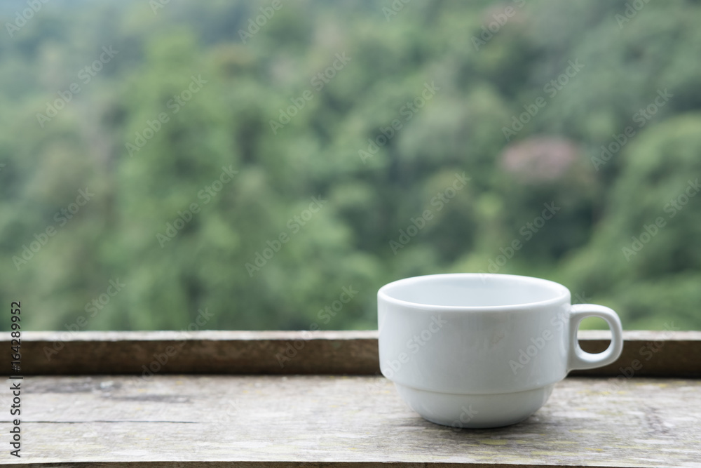 white tea cup on wood table with green nature background