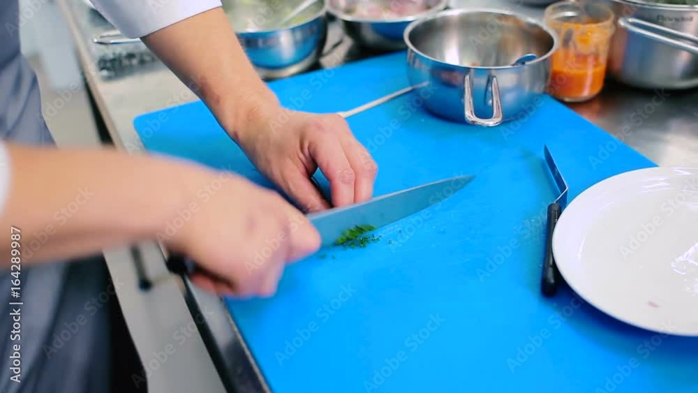 The cook cutting the asparagus on the board into a small pieces. The cook cutting the asparagus on the board into a small pieces.