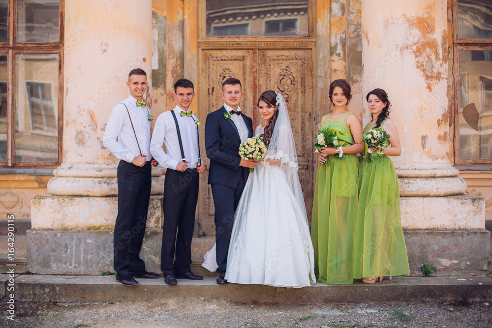 Newlyweds and their stylish friends pose before beautiful old ancient palace castle