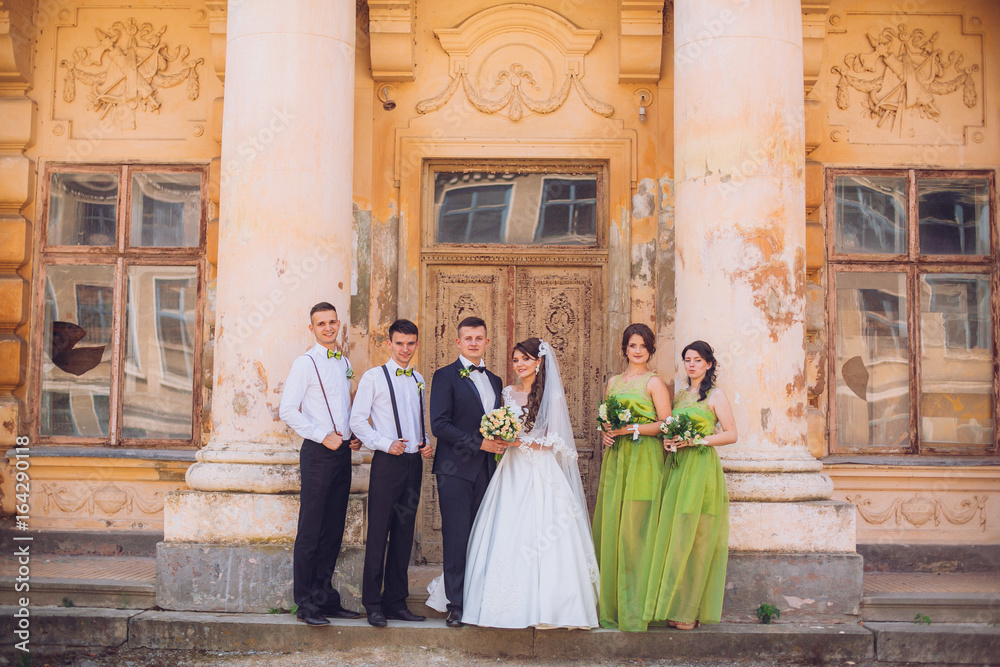 Newlyweds and their stylish friends pose before beautiful old ancient palace castle
