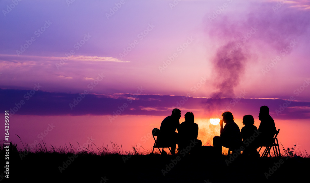 people sitting near campfire against sunset with copyspace - obrazy, fototapety, plakaty 