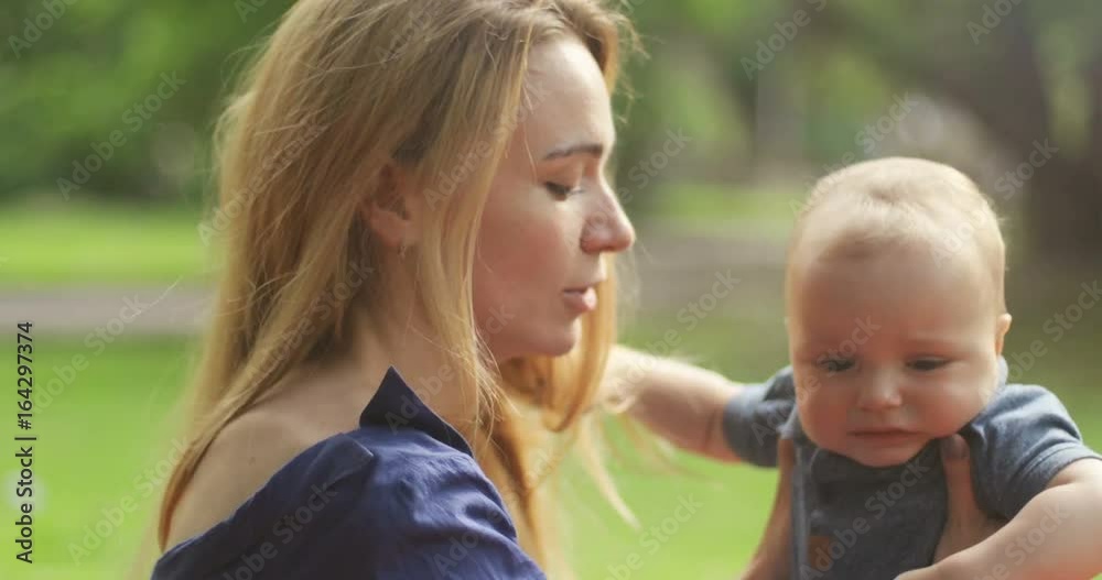 Young mother with her little son relaxing and playing in the park, mom trying to calm down crying baby, weekend together, lazy morning, warm and cozy scene. Selective focus. 4k Young mother with her little son relaxing and playing in the park, mom trying to calm down crying baby, weekend together, lazy morning, warm and cozy scene. Selective focus. 4k