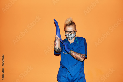 Nurse in blue uniform wearing gloves against orange wall photo