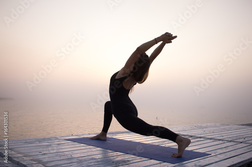 Fit woman in black sports wear posing in yoga asana on the beach