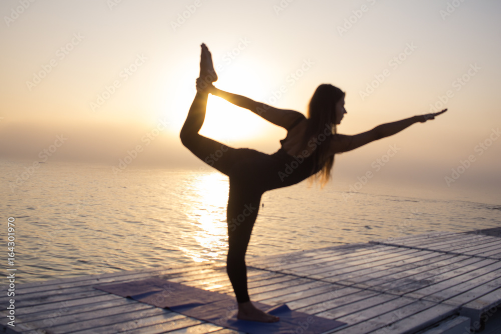 Young fit woman in black sportswear training yoga during the sunrise 