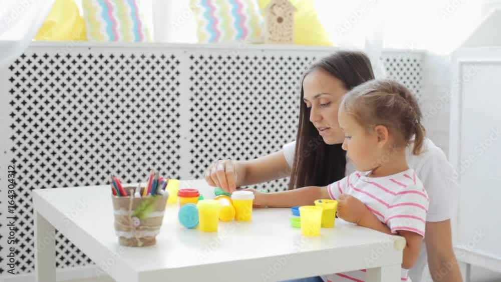 Mother with cute little daughter play with modeling clay at light living room. Mother with cute little daughter play with modeling clay at light living room.